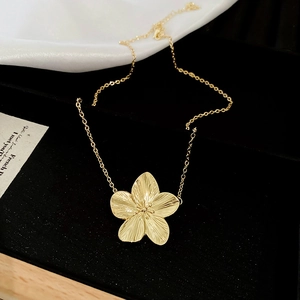 Close-up of golden flower pendant featuring fine radial brushed texture and cross chain