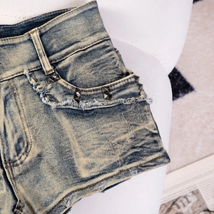 Detail von blauen Denim-Shorts mit Metallnieten und ausgefranstem Saum im Used-Look