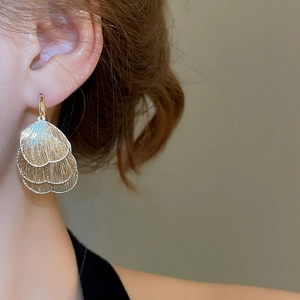 Close-up of layered gold leaf pendant earrings with textured finish on a model