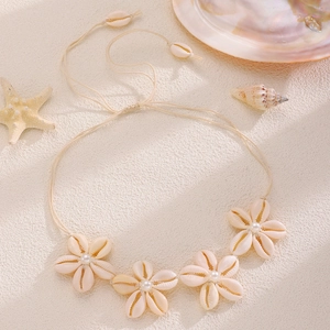 Collana artigianale di fiori di conchiglia con perle su sfondo sabbia e stelle marine