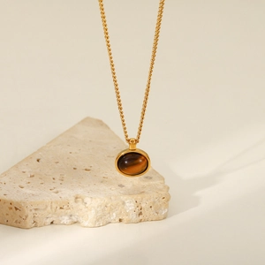 Macro view of 18K gold-plated chain with a round tiger eye stone pendant on a beige stone