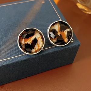 Macro shot of leopard print round stud earrings with faceted acrylic on a blue jewelry box