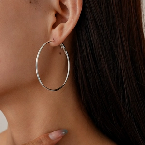 Close-up of a large silver hollow geometric hoop earring on a model's left ear