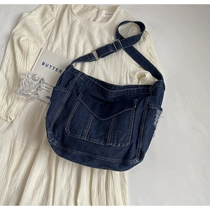 Détail d'un sac bandoulière en denim bleu avec poche à rabat et coutures sur tissu blanc