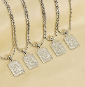 Detailed view of silver square letter pendants on round pearl chains over silk fabric
