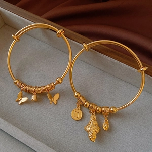 Detailed shot of two gold-plated bangles with traditional charms on grey velvet