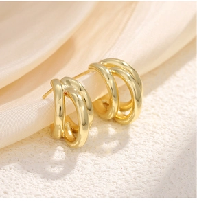 Macro detail of gold-tone triple-layered C-shaped metal hoop earrings on white silk