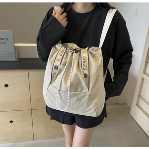 Detalle del bolso tote de lona beige con cierre de cordón y bordado de letras en la correa
