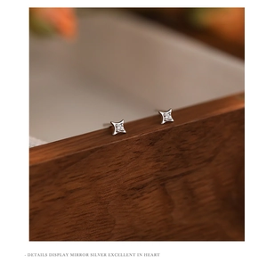 Macro shot of silver four-pointed star stud earrings with zircon inlay on walnut wood surface