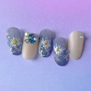 Floral nail art set featuring white daisies and blue rhinestones on matte blue and white nails