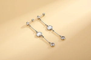 Close-up of silver tassel earrings with three descending clear crystals on a warm background