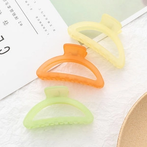 Three matte large hair claws in yellow, orange, and green on white textured fabric