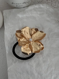 Detail of golden metal flower hair tie with pearl center on black elastic band