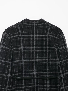 Detail view of the back of a dark gray plaid knit cardigan with black leather belt