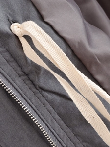 Detail of dark grey windbreaker featuring a metallic zipper and beige cotton drawstring