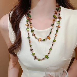 Detail of layered necklace featuring irregular green shells and natural stone beads
