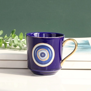 Ceramic Evil Eye coffee mug in navy blue with gold handle on elegant book stack