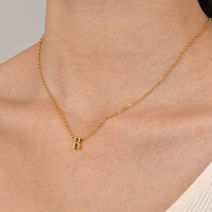 Detailed view of a gold R-letter pendant necklace worn on a delicate gold chain