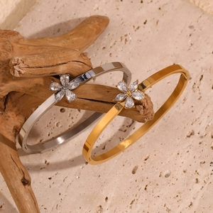 Detailed view of 18K gold and silver floral bangles with white crystals on a wooden branch