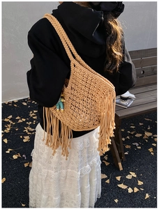 Detailed view of beige handmade woven tote bag with tassels on a casual outdoor model
