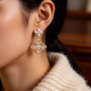 Close-up of pearl star and clover pendant earrings worn by a model in warm light