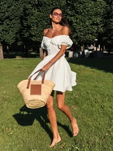 Detail eines weißen schulterfreien Kleides mit Puffärmeln und Strohtasche für den Sommer