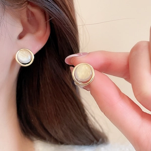 Macro shot of gold-plated stud earrings with round faux opal and smooth metallic texture
