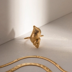 Artistic close-up of gold conch shell ring and matching necklace with ocean texture