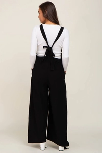Back view of black wide-leg maternity overalls paired with a white long-sleeve knit shirt