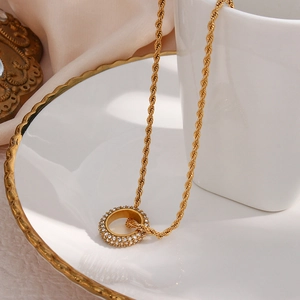 Gold twist chain necklace with sparkling zircon encrusted circle pendant on ceramic plate