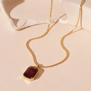 Detail of red rectangular gemstone pendant with gold chain and polished metal finish