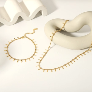 Detail of 18K gold tassel necklace and bracelet set on a white minimalist background