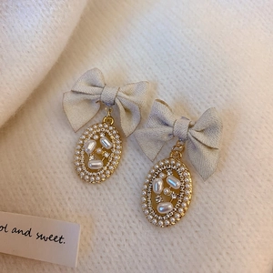 Detail of fabric bow pearl earrings with gold metal accents on soft knit background