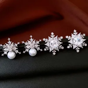 Sparkling snowflake stud earrings with crystals and pearl drops on a black leather stand