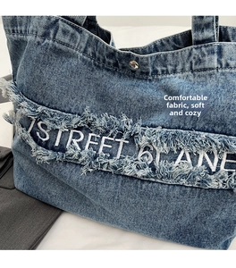 Détail du cabas en jean bleu avec bords effilochés et broderie de lettres blanches