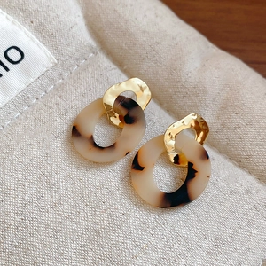 Detailed shot of leopard print acrylic and hammered gold circular earrings on linen fabric