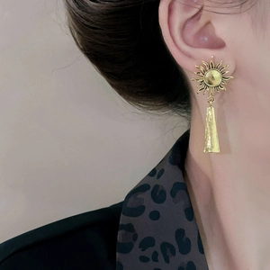 Détail d'une boucle d'oreille soleil dorée avec pendentif barre texturé sur un mannequin