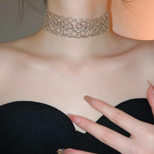 Gros plan d'un large collier ras du cou en maille dorée avec strass brillants sur un cou