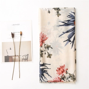 Flat lay of beige cotton linen scarf with red floral print and fringe edges on a table