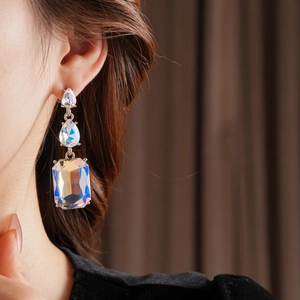 Close-up of dangling silver earrings with crystal droplets and rectangular stones on model