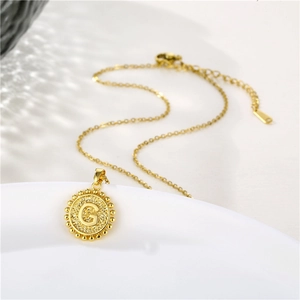 Macro view of gold round necklace with embossed letter G on a white ceramic plate