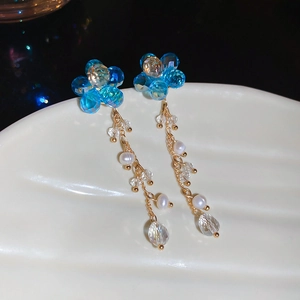 Detail of blue crystal flower earrings with dangling pearl tassels on a white shell plate