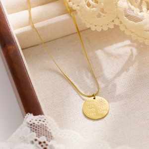 Détail du collier avec pendentif soleil gravé plaqué or 18k dans son coffret à bijoux
