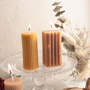 Primer plano de velas cilíndricas encendidas con rayas verticales sobre vidrio