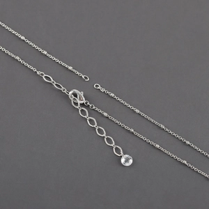 Detail of silver chain with lobster clasp and clear round charm on dark grey background