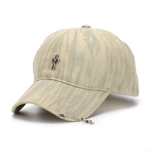 Close-up of a vintage denim baseball cap featuring a metal cross and safety pin detail