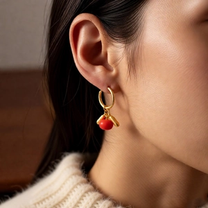 Detail of red persimmon drop earrings on model wearing a beige knitted sweater