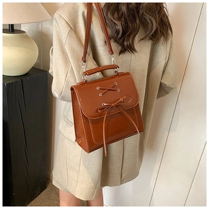 Detail of a brown leather backpack featuring a stylish front bow and crossbody straps