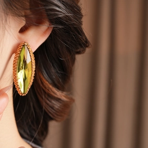 Detailed close-up of yellow-green marquise crystal earring with golden beaded edge