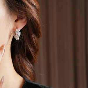 Close-up of a U-shaped silver earring with pearls and zircons worn on a model's ear